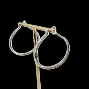 Puede incluir: Un par de pendientes de aro plateados con forma de l&aacute;grima, expuestos sobre un soporte dorado para pendientes sobre un fondo negro. Los pendientes tienen un acabado pulido y reflejan la luz.