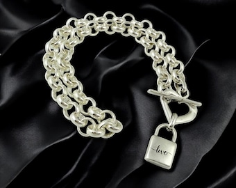 May include: A silver bracelet with a double chain design. The bracelet has a toggle clasp and a small padlock charm engraved with the word "love". The jewellery is displayed on a black background.