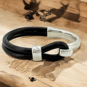 May include: A black leather bracelet with a silver clasp. The bracelet is double-layered and has a simple, minimalist design.