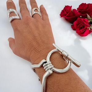 Massives, silbernes Armband mit geometrischem Muster, übergroßer Knebelverschluss mit großer Gliederkette, skulpturales Schmuckdesign