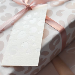 May include: A white gift tag with a pink and white leopard print design. The tag is tied with a pink ribbon to a gift wrapped in pink and white leopard print wrapping paper.