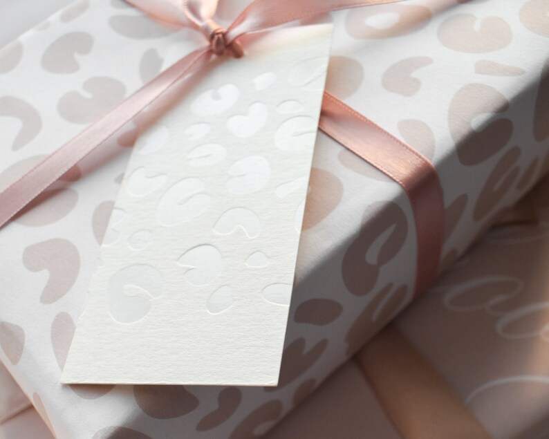May include: A white gift tag with a pink and white leopard print design. The tag is tied with a pink ribbon to a gift wrapped in pink and white leopard print wrapping paper.
