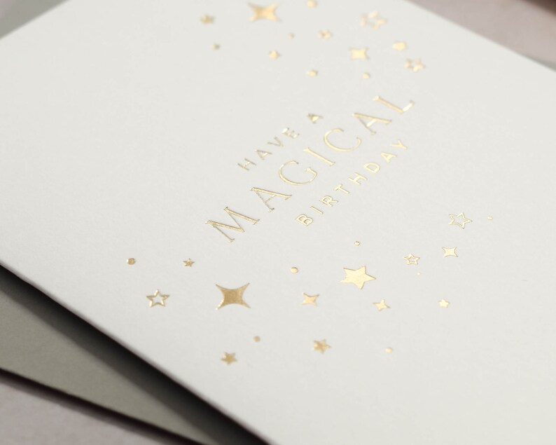 May include: White card with gold foil lettering that says "Have a Magical Birthday" with gold foil stars scattered around the text.