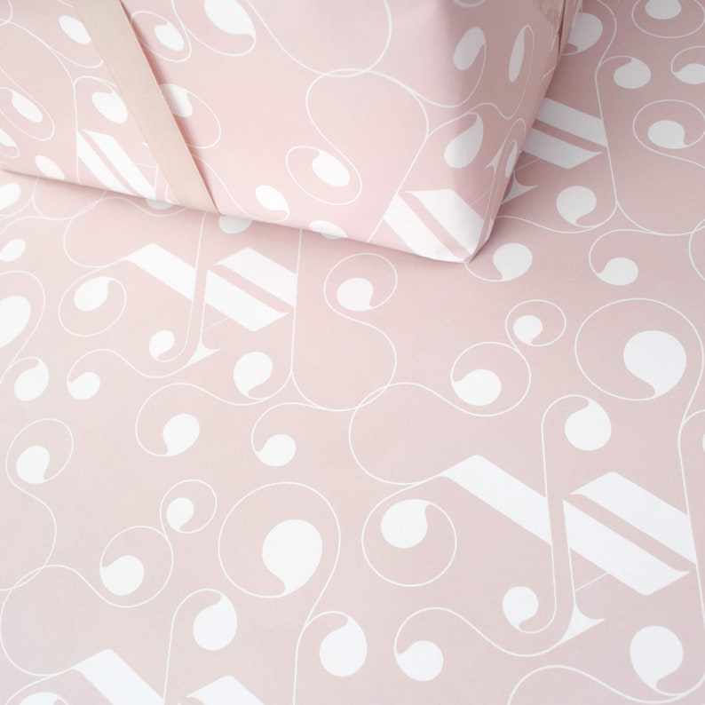 May include: Pink wrapping paper with a white geometric pattern. The pattern features swirls and circles.