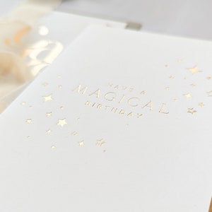 May include: A white card with gold foil lettering that reads "Have a Magical Birthday". The card is decorated with a scattering of gold foil stars.