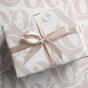 May include: A white gift box with a pink and white patterned design. The box is tied with a light brown satin ribbon.