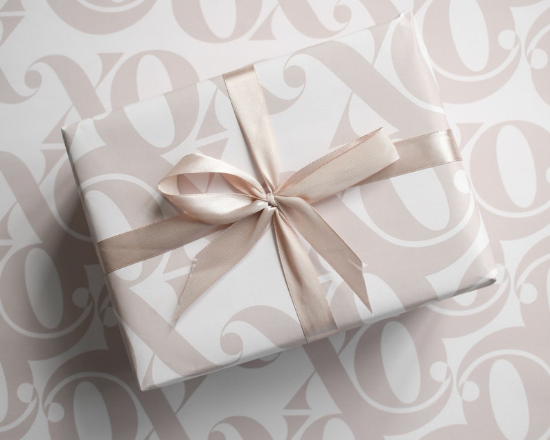 May include: A white gift box with a pink and white patterned design. The box is tied with a light brown satin ribbon.