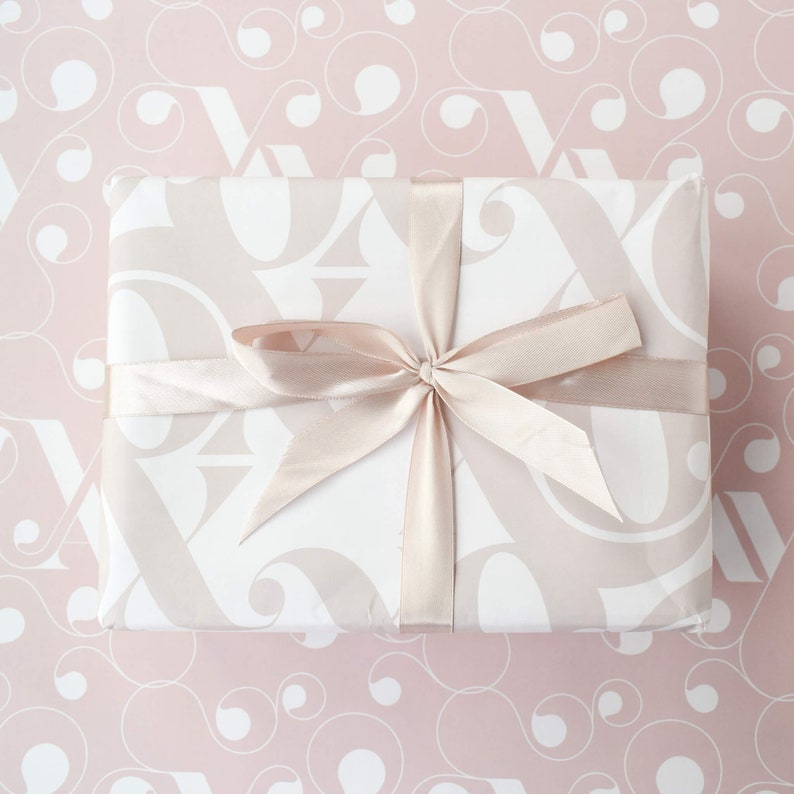 May include: A white gift box with a pink and white pattern is wrapped with a light pink satin ribbon. The box is tied with a bow.