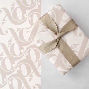 May include: A gift box wrapped in beige patterned paper with a brown satin ribbon tied in a bow. The paper has a repeating pattern of stylised letters.