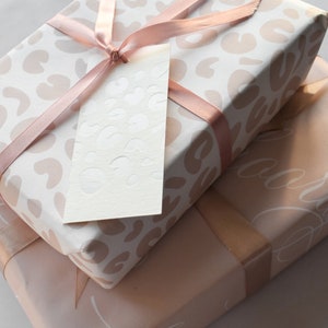 May include: Two gift boxes wrapped in pink and white patterned paper with a pink ribbon and a white gift tag. The top box has a leopard print pattern and the bottom box has a delicate floral pattern.