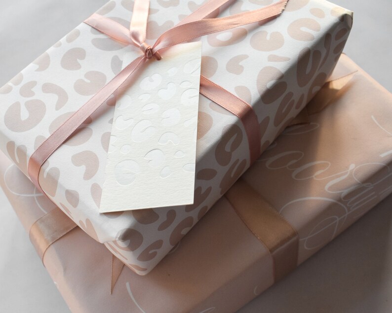 May include: Two gift boxes wrapped in pink and white patterned paper with a pink ribbon and a white gift tag. The top box has a leopard print pattern and the bottom box has a delicate floral pattern.