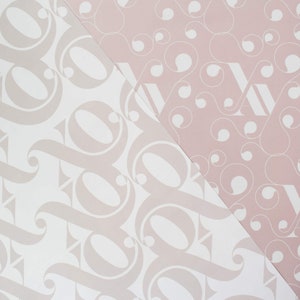 May include: Two pieces of wrapping paper with different patterns. One side is white with a light pink pattern of stylized letters. The other side is light pink with a white pattern of circles and swirls.