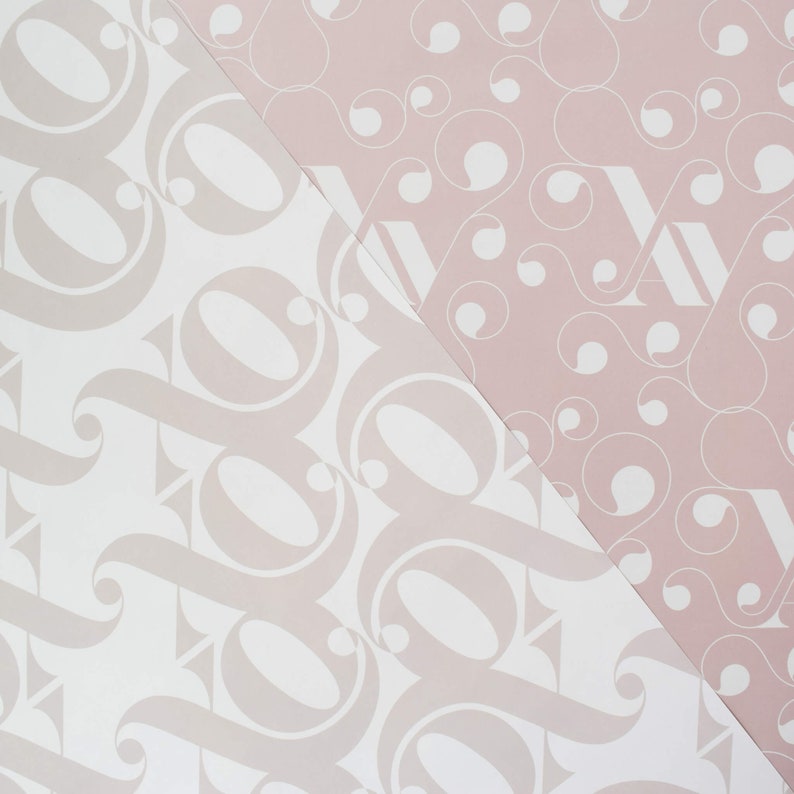 May include: Two pieces of wrapping paper with different patterns. One side is white with a light pink pattern of stylized letters. The other side is light pink with a white pattern of circles and swirls.