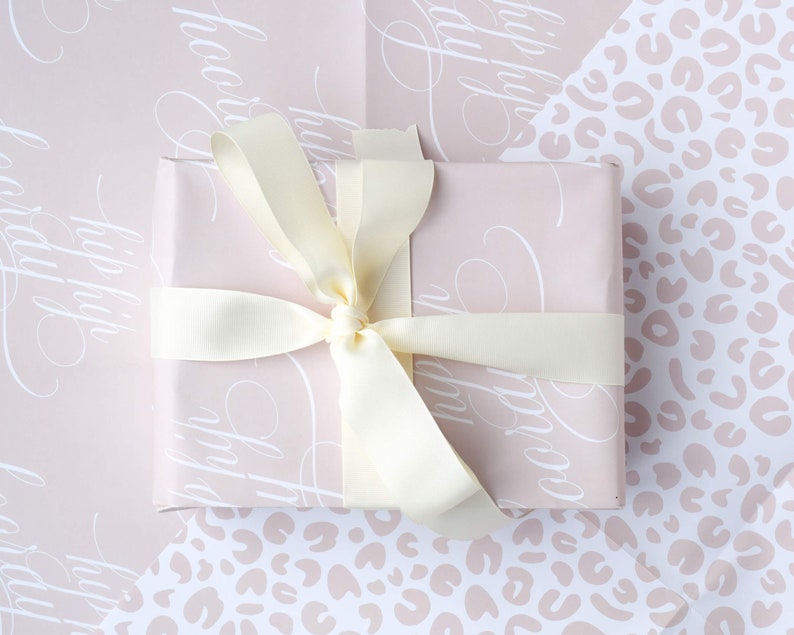 May include: A pink gift box with a white script pattern and a cream satin ribbon tied in a bow.