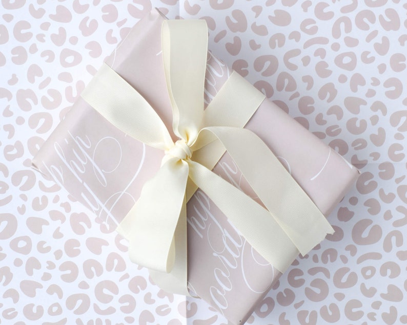 May include: A light pink gift box with a white leopard print pattern. The box is tied with a white satin ribbon and has the words "Happy Birthday" written on it in white script.