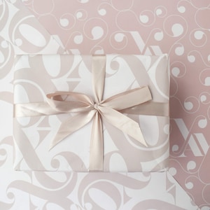 May include: A white gift box with a light pink and white patterned design. The box is tied with a light pink satin ribbon.