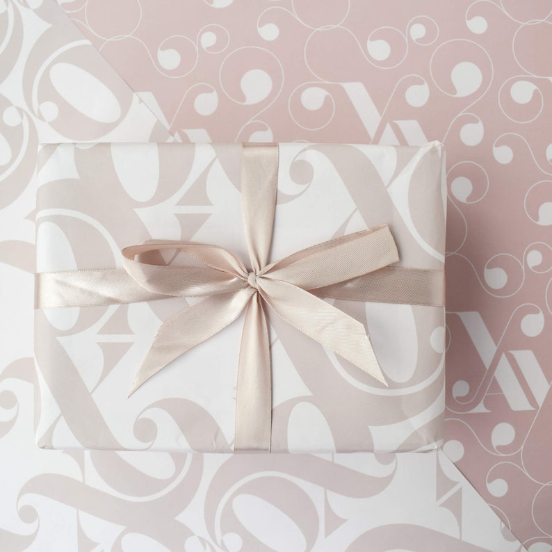May include: A white gift box with a light pink and white patterned design. The box is tied with a light pink satin ribbon.