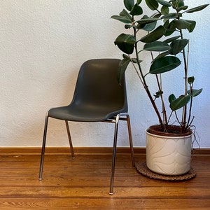 May include: A dark gray plastic chair with chrome legs sits on a wooden floor next to a potted plant with large green leaves.
