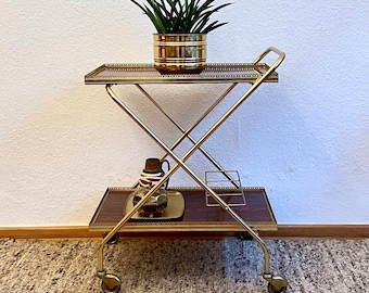 Neoclassical bar cart with a golden brass frame on wheels.