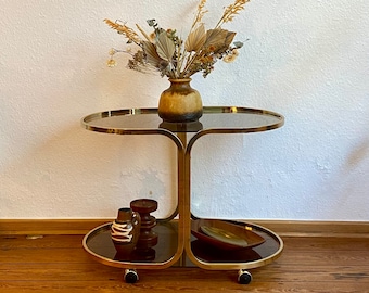 70s living room table with a golden brass frame and tinted glass tops on wheels.