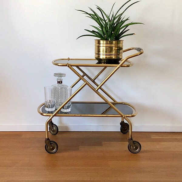 Italian bar cart with a gold metal rack and a wooden handle on rolls.