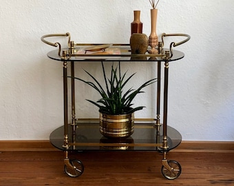 60s golden bar cart made of brass with two tiers of dark tinted glass on brass wheels.