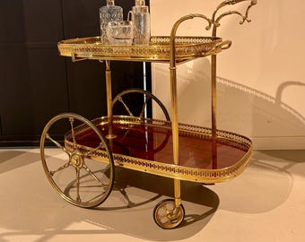 Gouden neoklassieke bartrolley van messing met twee mahoniehouten plateaus op wielen met rubberen banden.