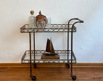 Art Deco 1930s golden bar cart with two tiers of glass on rubber-tired wheels.