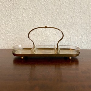 May include: A brass serving tray with three glass compartments and a handle. The tray has a polished finish and sits on four small feet.