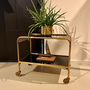 アールデコ調の 1930 年代の金色のバーカート。真鍮製で、ゴムタイヤの車輪に 2 段のガラスが付いています。