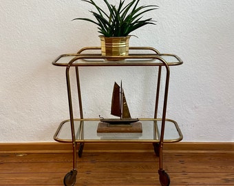 Art Deco 1930s golden bar cart made of brass with two tiers of glass on rubber-tired wheels.