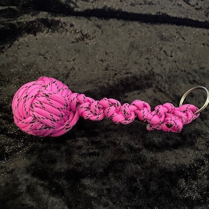 May include: A pink and black paracord keychain with a knotted ball at one end and a silver key ring at the other.