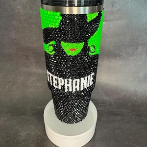 May include: A black and green stainless steel tumbler with a rhinestone design of the Wicked Witch of the West. The tumbler has a black lid and a white name "STEPHANIE" on the bottom.