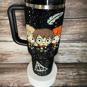 Puede incluir: Un vaso de acero inoxidable negro con temática de Harry Potter. El vaso está cubierto de diamantes de imitación y presenta un diseño de Harry Potter, Ron Weasley y Hermione Granger. El vaso también tiene un asa negra y una tapa negra con una pajita.