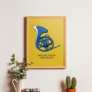 Op de afbeelding: Een ingelijste print met een blauwe Franse hoorn illustratie op een gele achtergrond. De tekst "I WOULD HAVE STOLEN YOU A WHOLE ORCHESTRA" staat eronder. De print zit in een houten lijst en wordt op een houten oppervlak getoond.