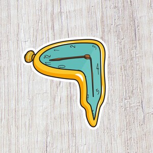 May include: A sticker depicting a melting clock in a surrealist style. The clock face is teal with black numerals and hands, encased in a gold-coloured frame. The clock's form is distorted, as if it is melting downwards.