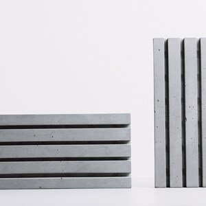 May include: Two rectangular concrete blocks with a series of vertical grooves. The block on the left is lying flat, while the block on the right is standing upright.