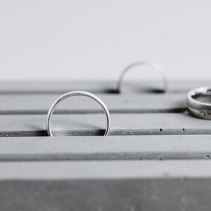 May include: A gray concrete ring holder with two silver rings resting in the grooves.