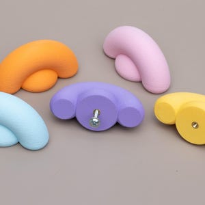 May include: Five colorful cabinet knobs in shades of orange, pink, purple, yellow, and blue. Each knob has a unique, rounded design with a screw for easy installation. These decorative knobs add a pop of color to any furniture piece.