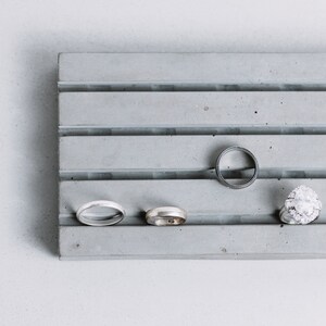 May include: A gray concrete ring holder with four slots. There are four rings in the slots, two silver and two gold.
