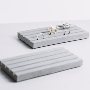 May include: Two gray concrete ring holders. The top holder has five rings on it, including a gold ring with a unique design.