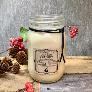 May include: A clear glass mason jar candle filled with off-white wax, featuring a black string tied around the rim. The label reads frederick candle company & Apothecary, SCENT name, 16oz/454g, and 80 hrs. burn time with a flame icon.