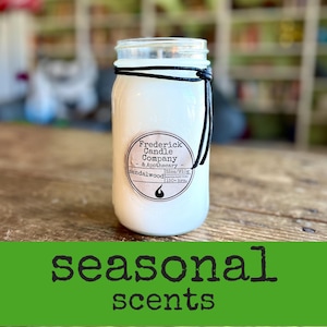May include: A white candle in a clear glass jar with a black cord tied around the neck. The label reads Frederick Candle Company & Apothecary, sandalwood, 32oz/910g, and 150+ hrs. The text seasonal scents is displayed in black on a green background.