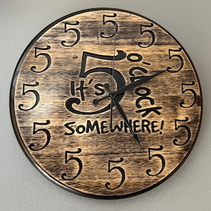 May include: A wooden clock with black hands and the text "It's 5 o'clock somewhere!"  The clock face is surrounded by the number 5 in a decorative font.