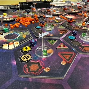 May include: A close-up view of a game board with hexagonal tiles, colorful dice, and miniature spaceships. The board is set up for a game of space exploration and combat.