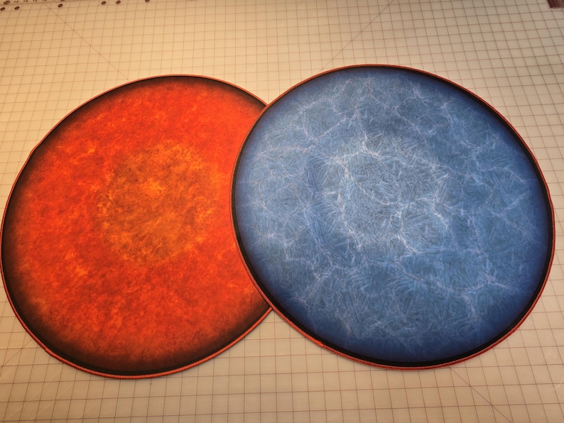 Peut inclure: Deux plateaux de jeu ronds et plats. Un plateau est orange et rouge avec une bordure brun fonc&eacute;. L'autre plateau est bleu avec un motif marbr&eacute; blanc et une bordure brun fonc&eacute;.