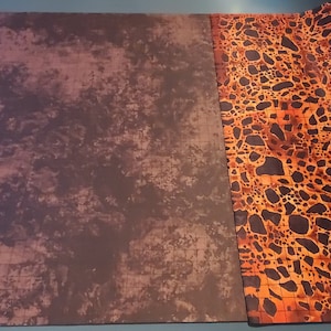 May include: A large, rectangular, brown and orange gaming mat with a grid pattern. One side of the mat has a textured, mottled brown surface. The other side has a repeating pattern of orange and black spots.