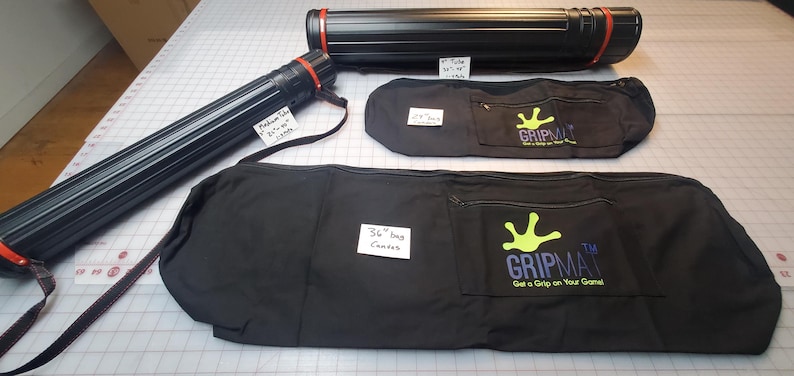 Peut inclure: Trois sacs en toile noire avec des tubes t&eacute;lescopiques rouges et noirs. Les sacs ont un logo de main verte avec le texte "The Gripmat Get a Grip on Your Game". Les tubes sont &eacute;tiquet&eacute;s &agrave; la main indiquant leur taille : "Medium Tube 18" x 24" x 1/2", "36" Inch Canvas", et "36" Tube 18" x 48" x 1/2".