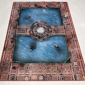 以下が含まれることがあります： 中央に円形のデザインが施された赤と青のゲームマット。マットはグリッドパターンと青い水のようなデザインが特徴です。