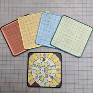 Könnte beinhalten: Eine Sammlung farbenfroher Spielmatten und eine Brettspielmatte. Die Matten sind quadratisch mit Rastermustern in verschiedenen Farben: Braun, Gelb, Blau und Grün. Die Brettspielmatte hat ein spiralförmiges Design mit blauen Knöpfen.
